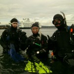 Three scuba divers in water near ferry.