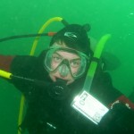 Scuba diver underwater in green murky water.