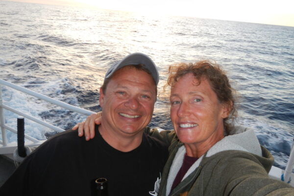 Couple smiling on a boat at sea during sunset.