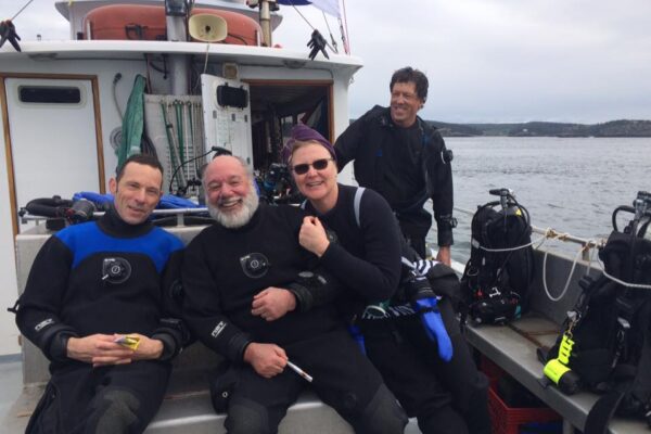 Divers smile on boat with scuba gear.