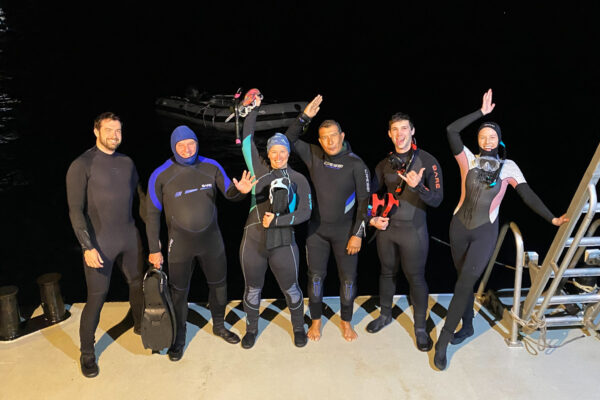 Divers in wetsuits posing on a dock at night.