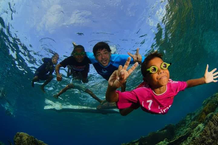 Children swimming underwater, showing peace signs.