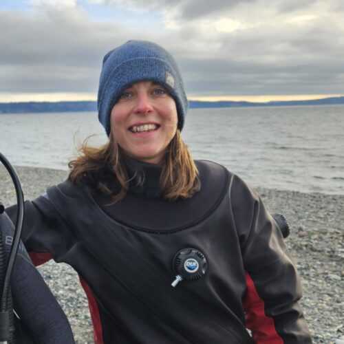 Smiling person in wetsuit by the ocean.