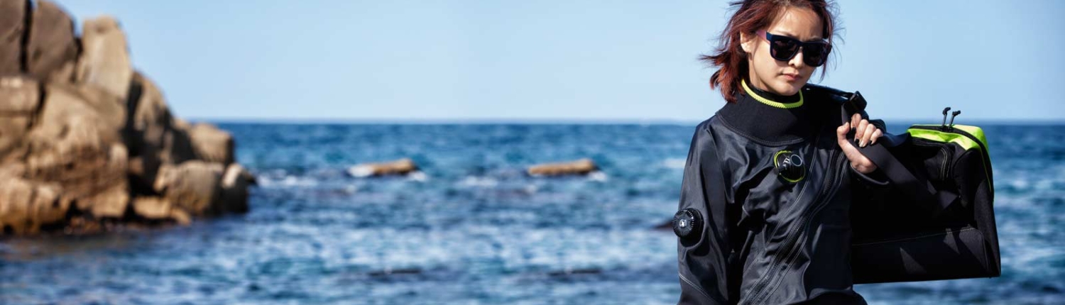 Woman in wetsuit by the ocean on rocky beach.