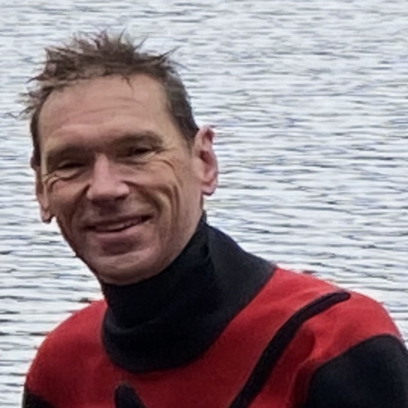 Person smiling in a red wetsuit by water