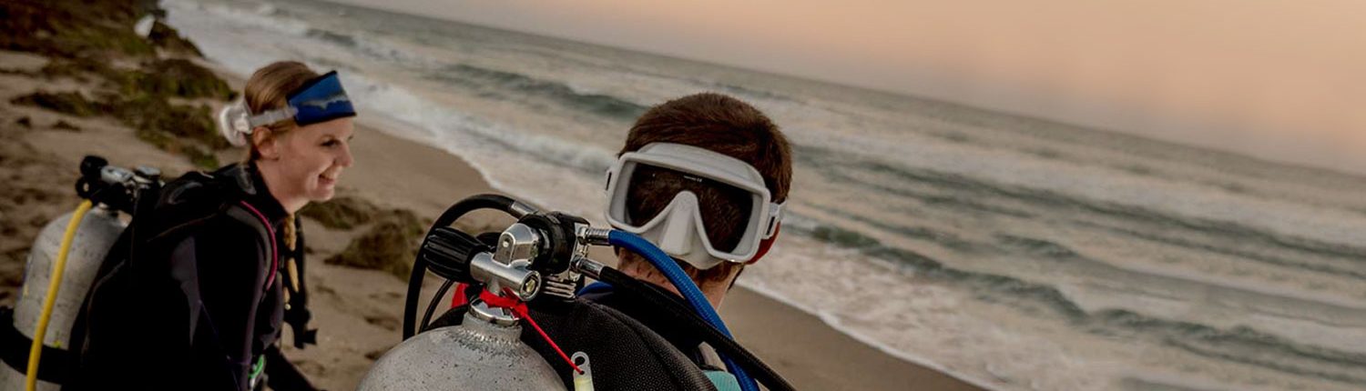 Divers preparing on a beach at sunset.