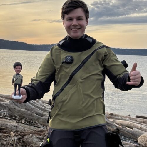 Person holding a mini figure, smiling at lakeside.