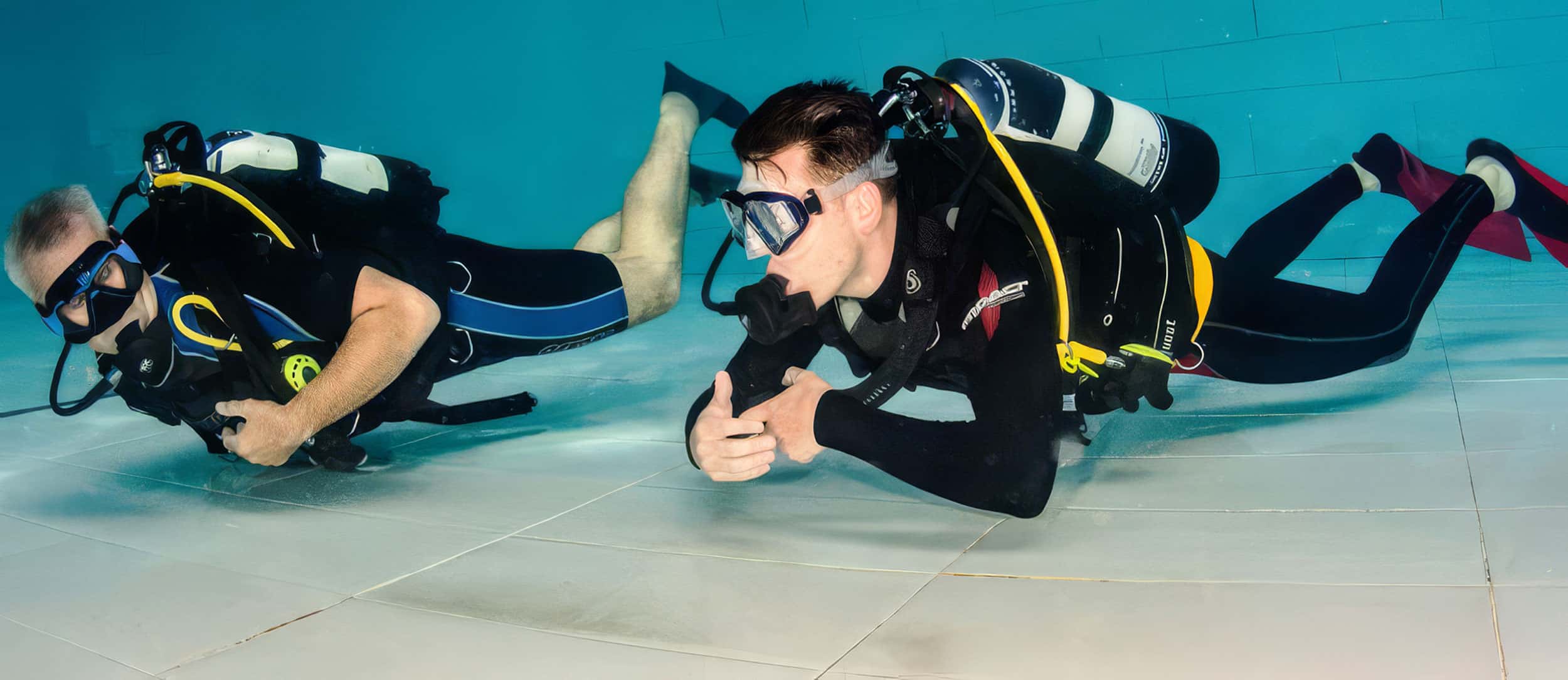 Two divers practicing underwater in a swimming pool.